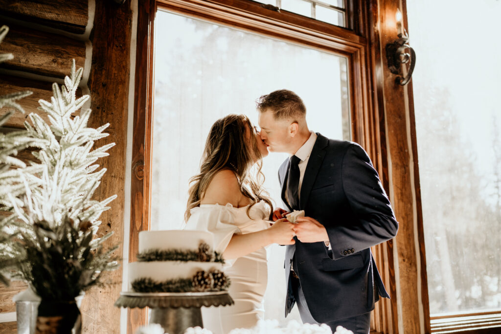 Mountain Elopement with a warm and moody edit. They are standking in front of a cake kissing. 