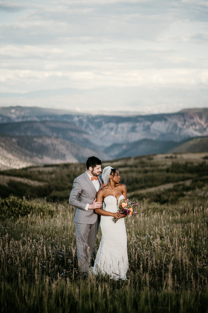 Interracial couple in Colorado mountains. Husband embracing wife and kissing shoulder